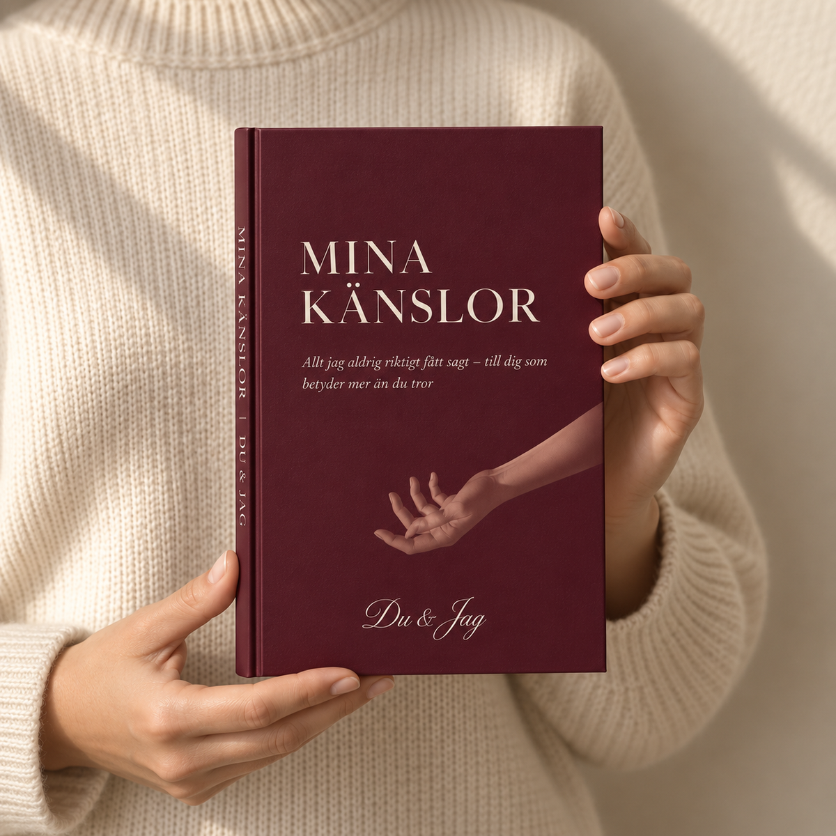 Kvinna håller upp Mina Känslor framför en gräddvit stickad tröja